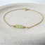 A product shot showing a peridot bracelet. The bracelet shows three faceted peridot roundels with one delicate gold bead on each end lined up on a dainty gold cable chain. The dainty bracelet is displayed on a stoneware dish.