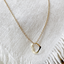 A gold heart charm necklace displayed on fabric.