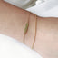 up close model shot of arm wearing a dainty gold rolo chain bracelet stacked with a beaded peridot chain bracelet