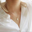 Model is wearing a delicate gold chain necklace with a small, oval gold Mother Mary pendant showing the back of the charm featuring an M with a cross above surrounded by tiny stars and dainty hearts.