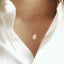Model is wearing a delicate gold chain necklace with a small, oval gold Mother Mary pendant.