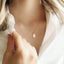 Model is wearing a delicate gold chain necklace with a small, oval gold Mother Mary pendant.