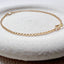 A bezel set crystal centered on a dainty rolo chain bracelet displayed on a stoneware jewelry dish