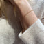 A model is wearing a gold Figaro chain bracelet with a cozy cashmere sweater.