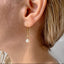 Close-up of an ear wearing a gold earring with an opal drop.