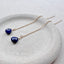 Gold chain earrings with blue sapphire gemstones on a white stone surface