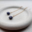 Gold earrings with blue sapphire gemstones on a white stone surface