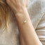 Delicate gold bracelet with white opals on a wrist against a neutral background