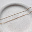 A dainty gold cable chain bracelet and minimalist flat cable chain bracelet displayed on a stoneware jewelry dish