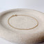 A dainty gold cable chain bracelet displayed on a stoneware jewelry dish