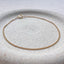 A dainty gold curb chain bracelet displayed on a stoneware jewelry dish