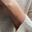 A dainty gold curb chain bracelet displayed on a model wearing a cozy cashmere sweater