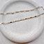 A dainty gold dapped chain bracelet and a dainty gold Figaro chain bracelet displayed on a stoneware jewelry dish