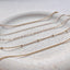 a bracelet stack of a gold rolo chain bracelet, dainty gold cable chain bracelet, gold minimalist flat cable chain bracelet, gold satellite chain bracelet and gold flat curb chain bracelet displayed on a stoneware jewelry dish