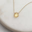 Gold necklace with a yellow citrine gemstone pendant on a white background