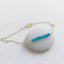 Gold bracelet with turquoise beads on a white stone surface