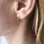 Close-up of an ear wearing a gold hoop earring with blonde hair partially visible.