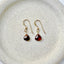 Gold earrings with red garnet gemstones on a beige plate.