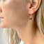 Close-up of a woman wearing a pair of earrings with red gemstones.