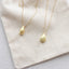 Gold teardrop pendant necklaces on a textured beige surface