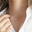 The model is shown holding a dainty gold heart charm necklace.