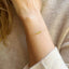 A model is shown wearing a dainty peridot bracelet. The bracelet shows three faceted peridot roundels with one delicate gold bead on each end lined up on a dainty gold cable chain. 