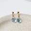 a pair of gold ball stud earrings with dangling teardrop faceted aquamarine gemstones