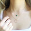 A model is wearing an emerald heart shaped necklace layered with a minimalist circle necklace sold together as a layered necklace set.
