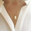 Gold necklace with a rectangular initial tag pendant with citrines on a person wearing a white blouse.
