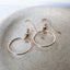 Dainty gold circle drop earrings shown reflecting light
