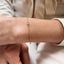 A bezel set crystal centered on a dainty rolo chain bracelet displayed on a model