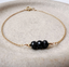 Dainty black onyx gold chain bracelet worn with a knit sweater