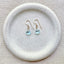 Gold filled blue topaz drop earrings with faceted gemstone pendants displayed on stone dish