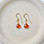 Pair of gold-filled carnelian heart drop earrings on a cream stoneware dish