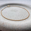 A dainty gold curb chain bracelet displayed on a stoneware jewelry dish