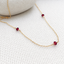 Three faceted garnet beads wire-wrapped on a gold-filled chain on white woven fabric