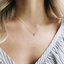 Model wearing a minimalist prehnite teardrop necklace in 14k gold-filled with a striped blouse