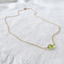Close-up of a wire-wrapped faceted peridot bead on a delicate gold chain
