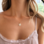 Gold initial disc necklace with opal charms worn on the collarbone