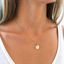 Gold initial disc necklace with opal teardrop worn with a white top, October birthstone