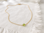 Dainty gold peridot necklace laid out on a fringed white linen cloth