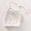 Gold opal necklace on a clear crystal block with a textured white background