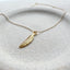 Gold feather necklace on a textured white surface