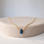 Deep blue London topaz teardrop pendant on a dainty gold-filled chain on a cream display pedestal