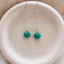 Emerald threader earrings in sterling silver with faceted emerald briolette drops on a fine chain, on a speckled ceramic dish
