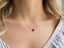 Model wearing a dainty garnet teardrop necklace in 14k gold-filled with a striped blouse
