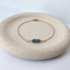 Minimalist gold-filled London blue topaz bracelet with three dark blue faceted gemstone beads on an ivory dish