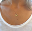 Dainty gold ruby initial pendant worn on the décolletage with a white tee