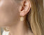 Close-up of a person wearing a gold earring with a citrine gemstone.
