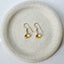 Gold citrine earrings on a textured stone plate with a light background
